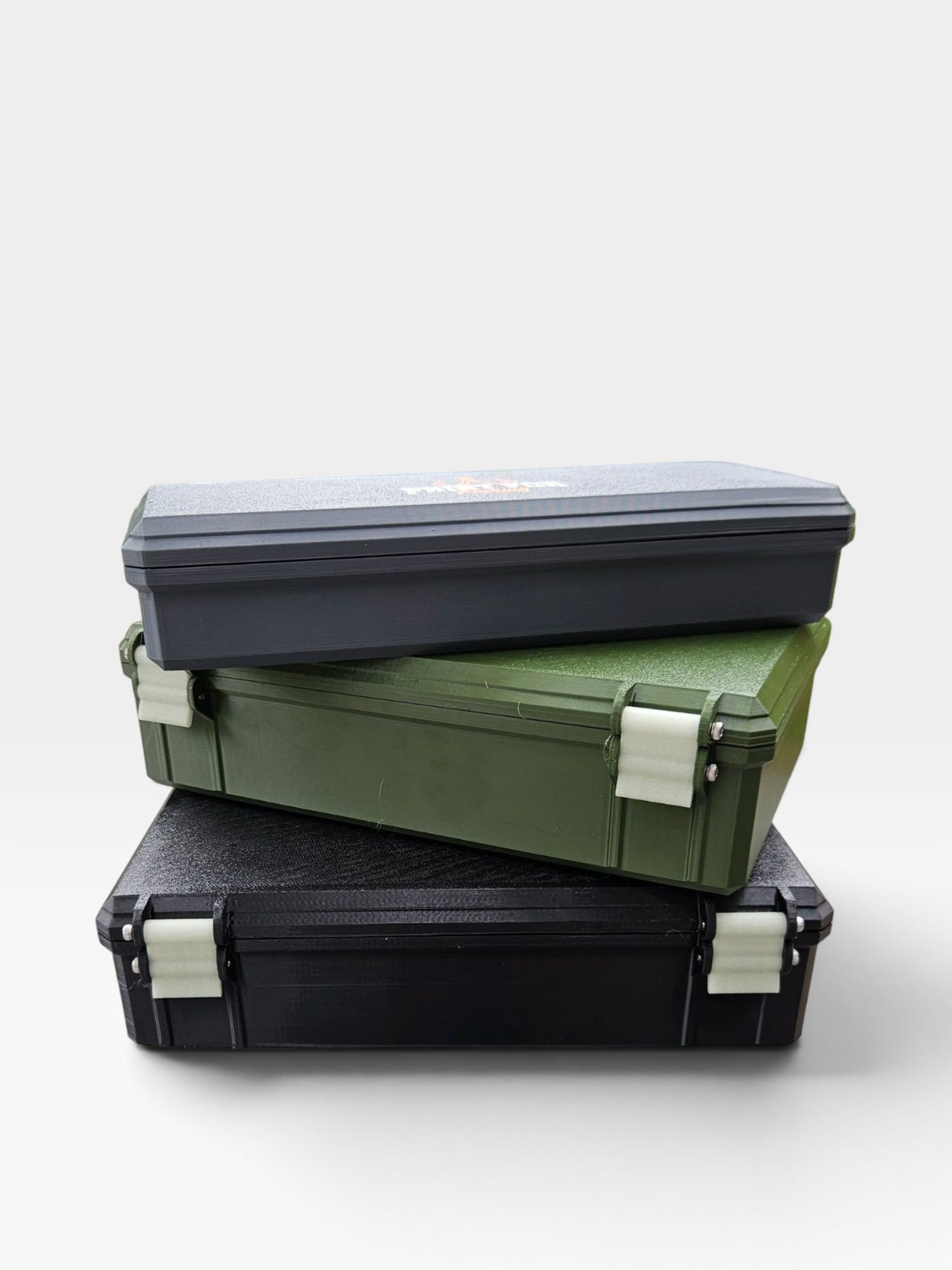 Trois boîtes à pêche PrintForFishing empilées, de couleurs noire, verte et grise, avec fermetures phosphorescentes.